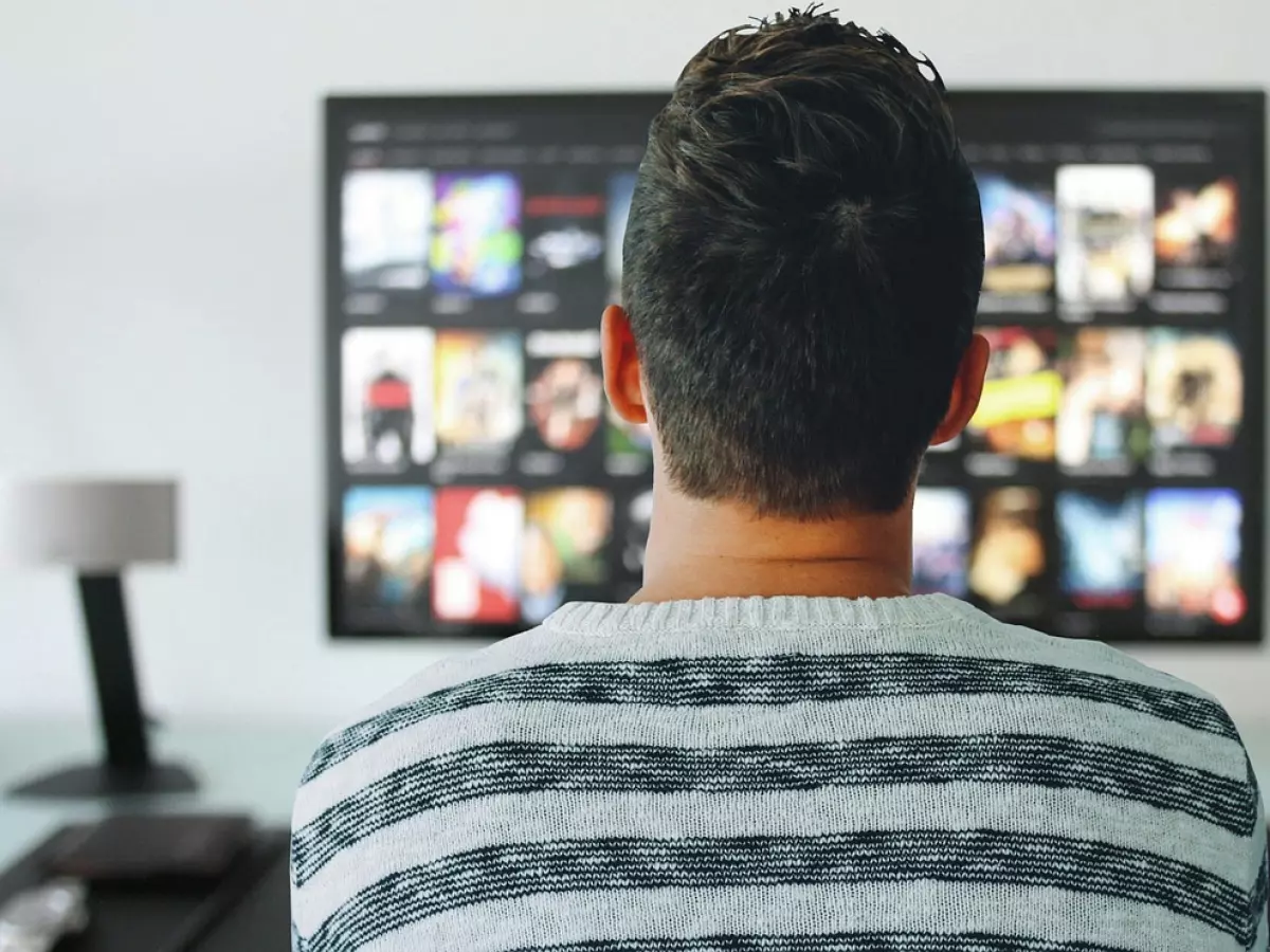 A man sitting in front of a large screen, looking at the content being displayed. The screen shows a variety of videos.